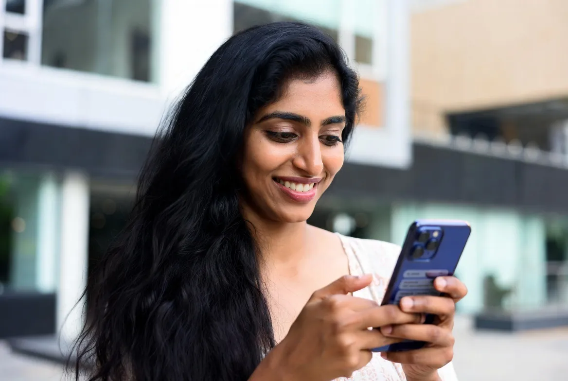 Woman smiling while using a tamil chat app outdoors
